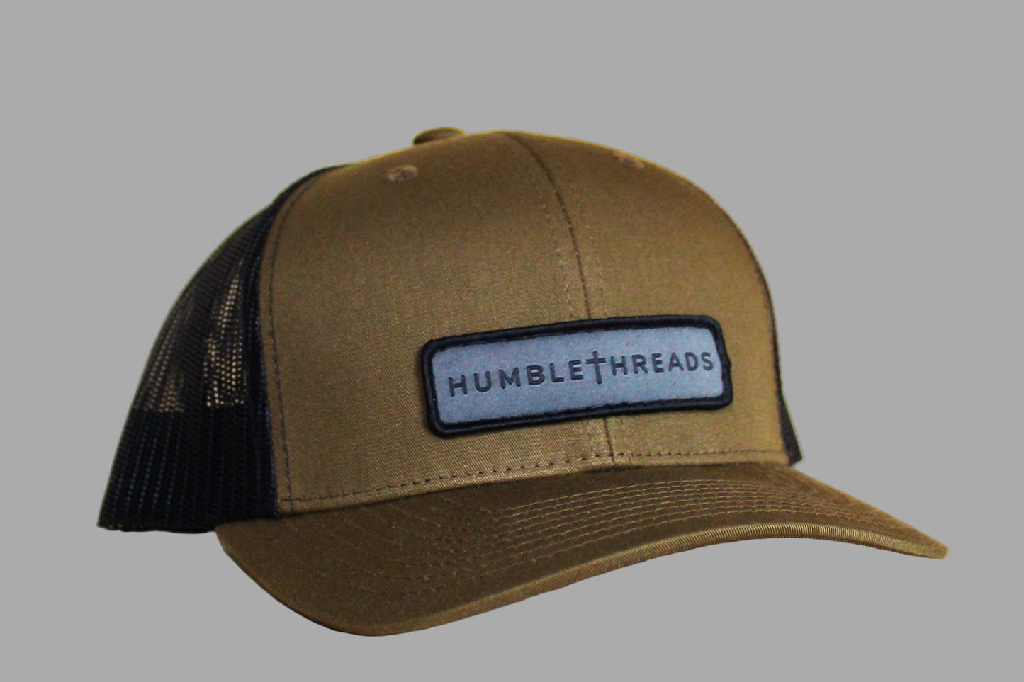 Green trucker cap with black mesh back and 'Humble Threads' logo on a light wooden surface.