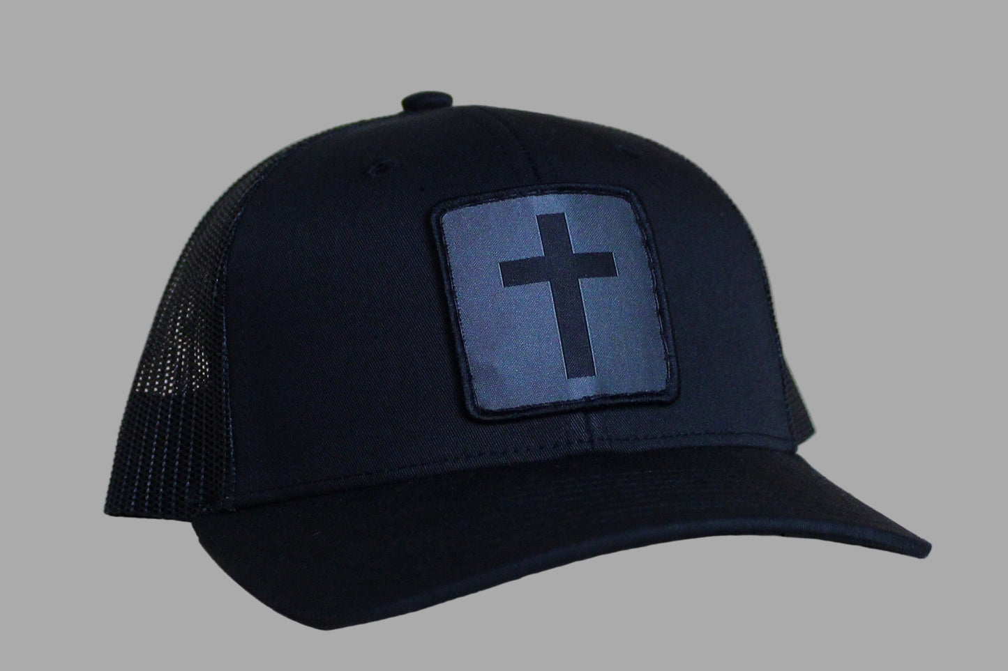 Black trucker cap with a cross patch on a light wood background
