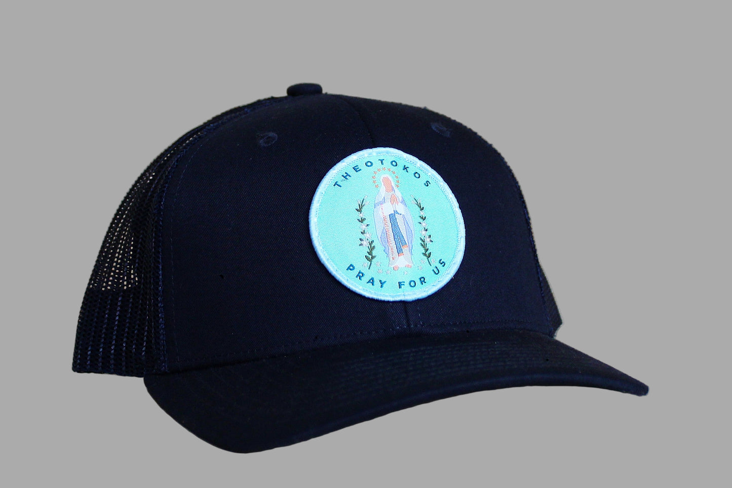 Black cap with a circular patch featuring an image of a religious figure on a wooden surface
