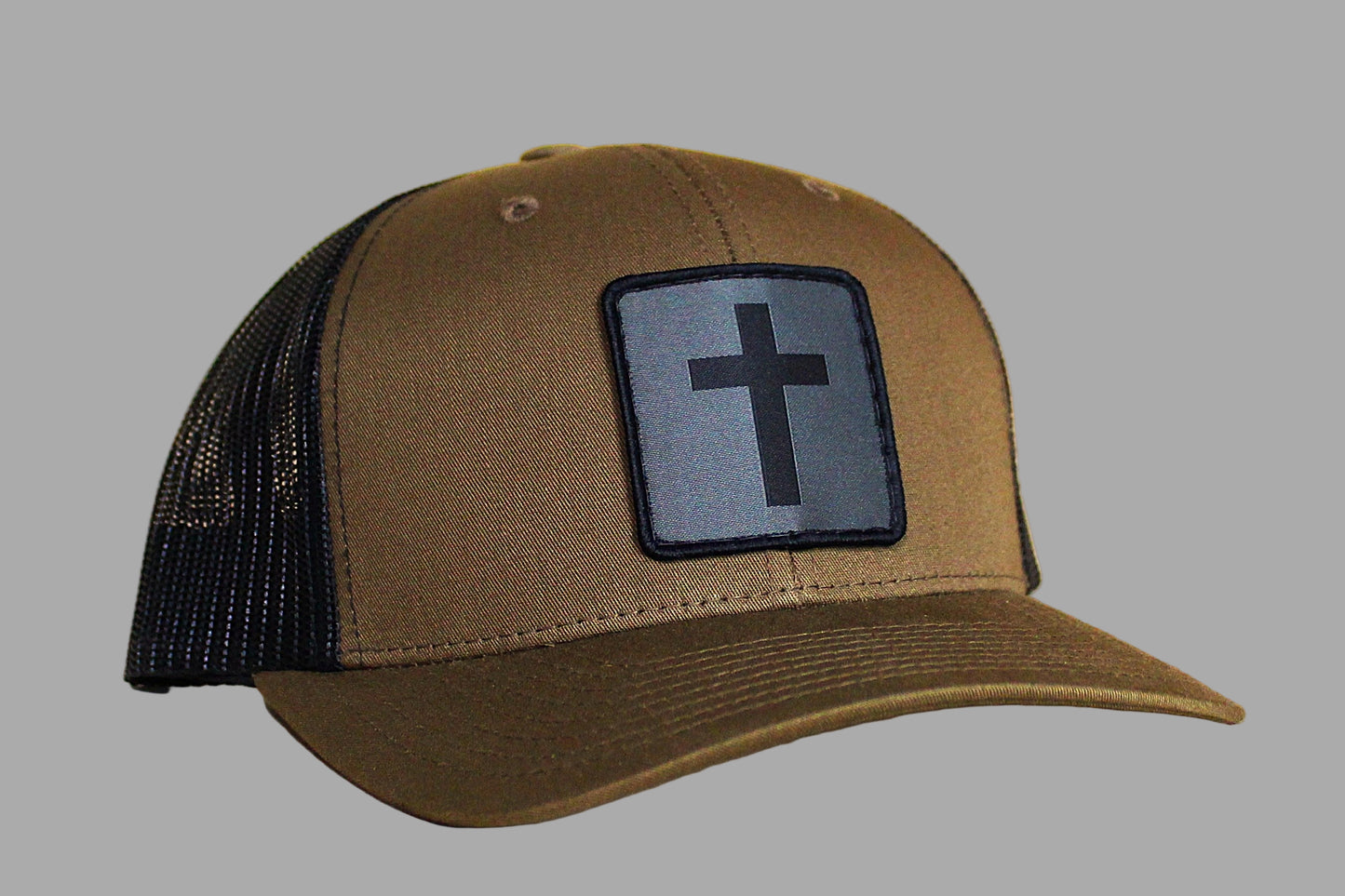 Brown cap with black mesh back and cross patch on a wooden surface