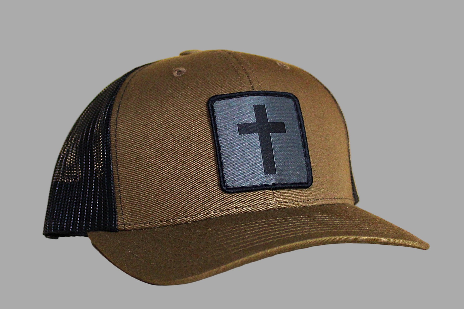 Brown cap with black mesh back and cross patch on a wooden surface