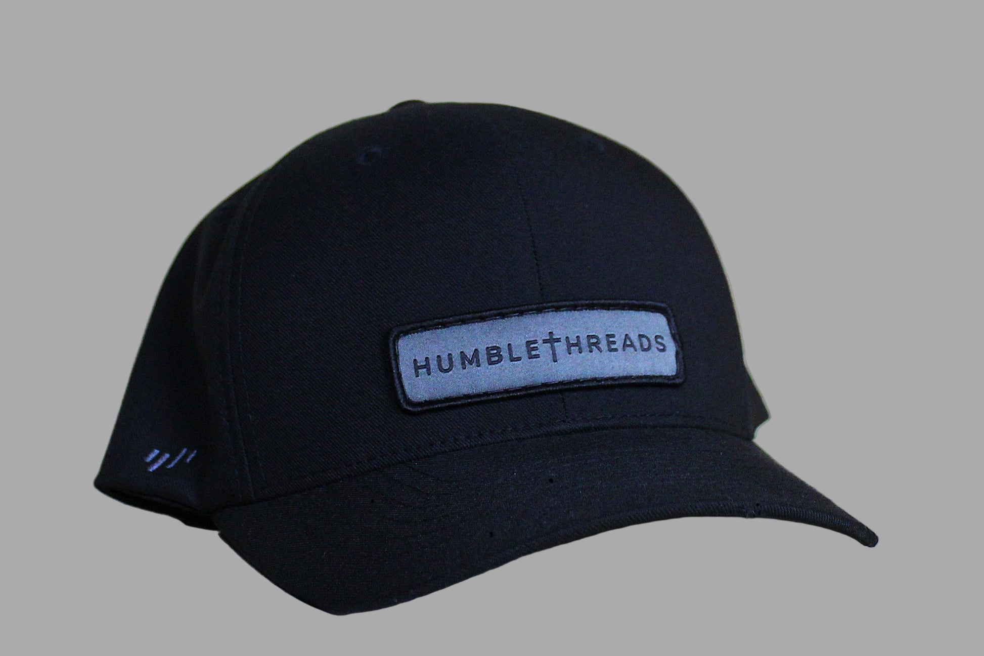Black cap with 'Humble Threads' logo on a light wooden surface