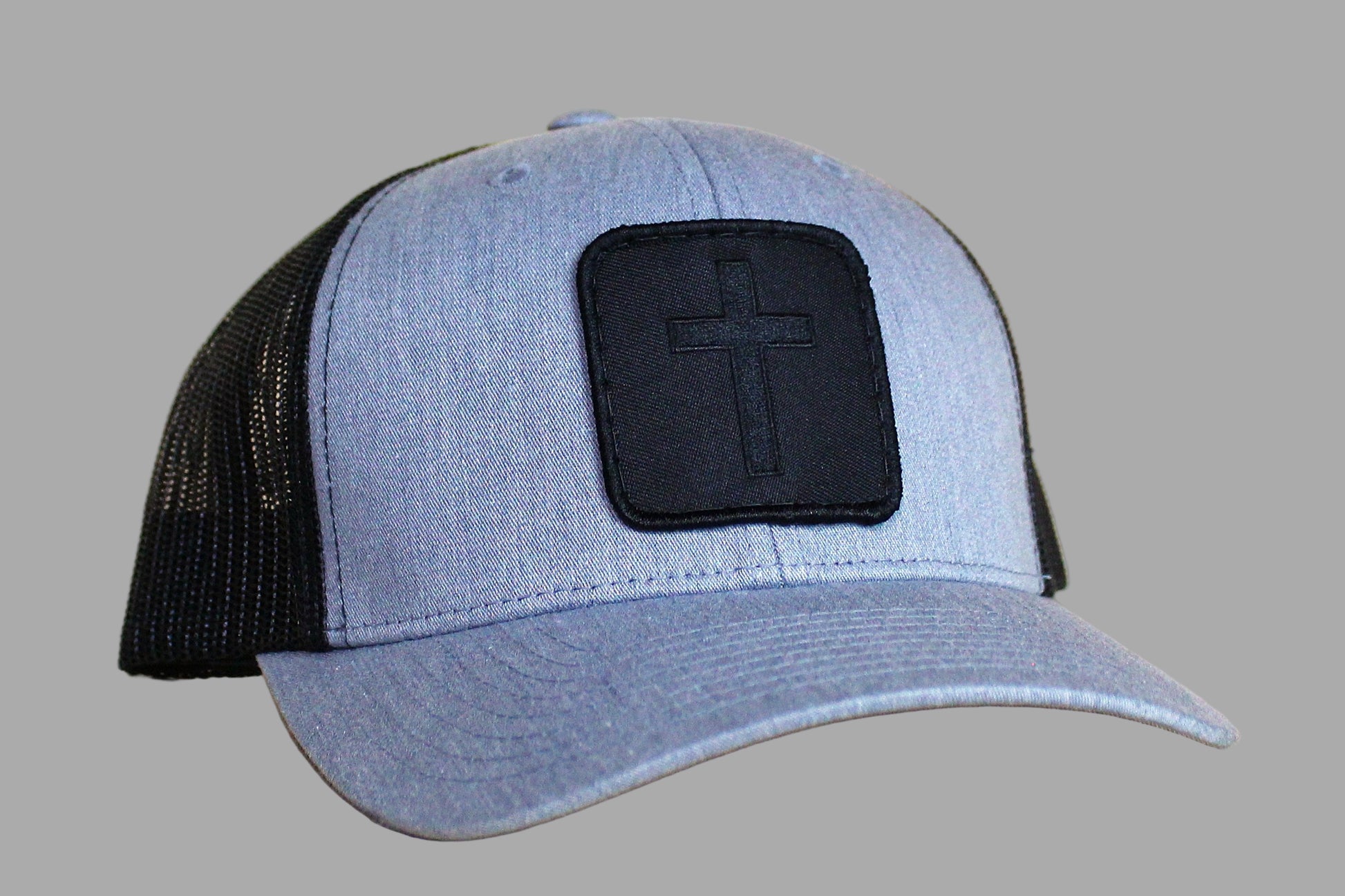 Blue and black trucker cap with a cross emblem on a light wood surface.