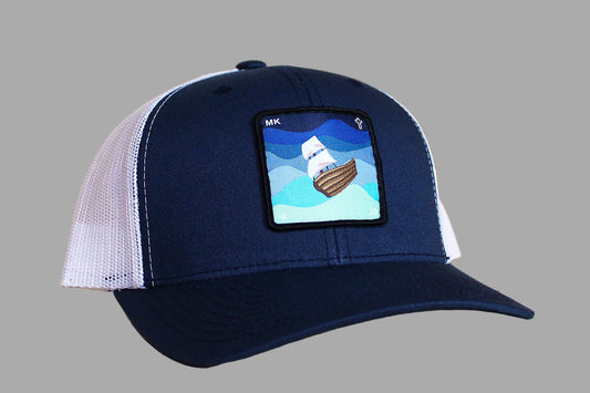 Navy blue cap with white mesh back and ship patch on a wooden surface