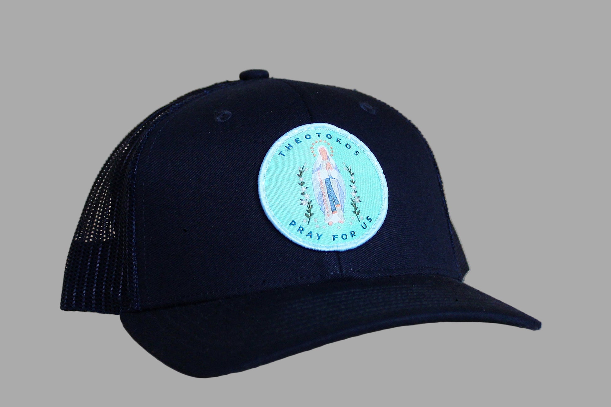 Black cap with a circular patch featuring an image of a religious figure on a wooden surface