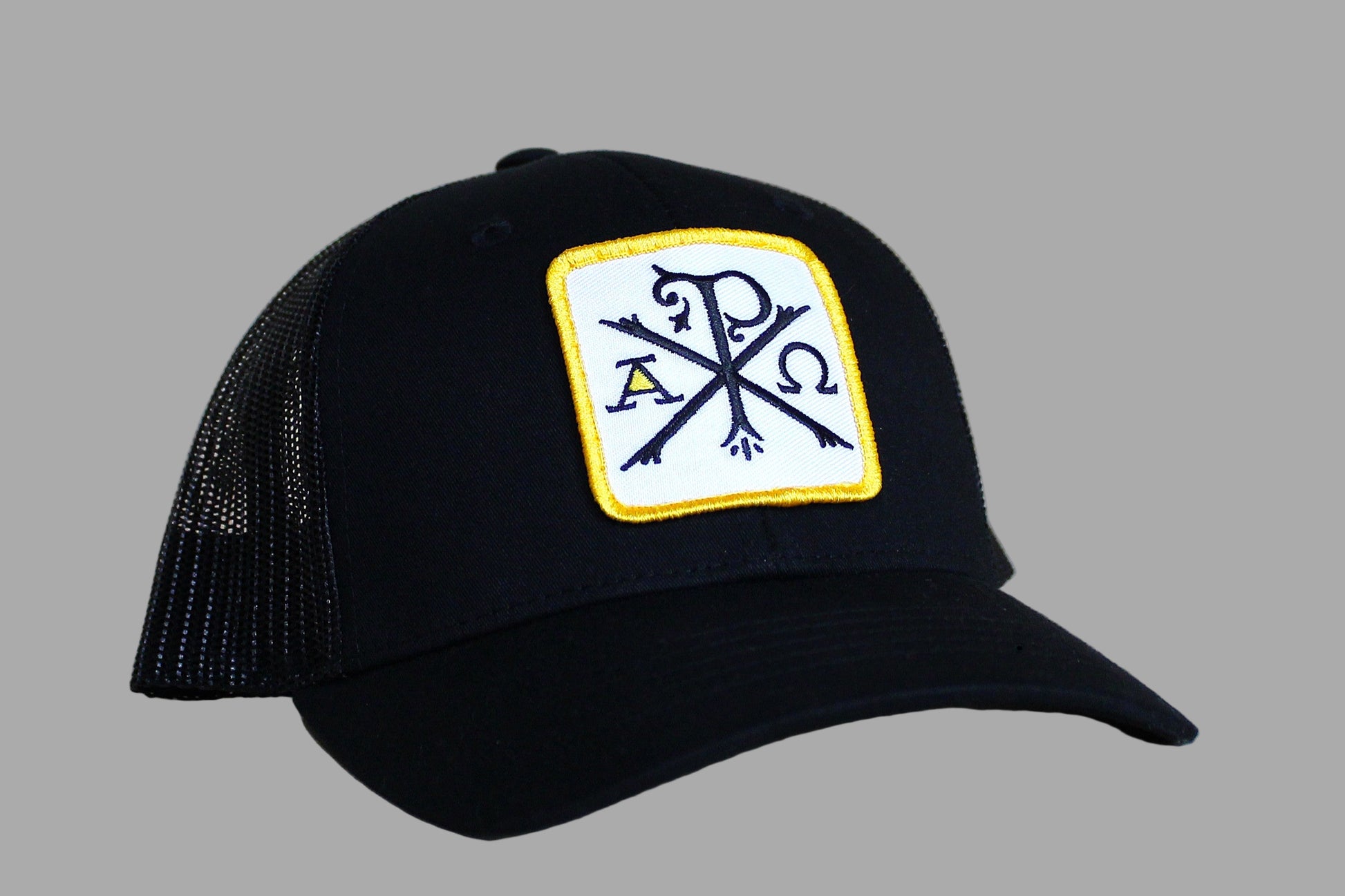 Black cap with a yellow and white patch featuring symbols on a light wood background