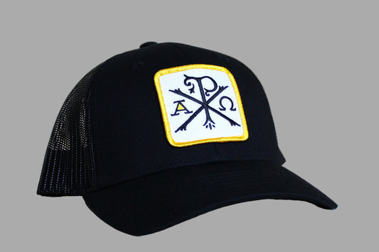 Black cap with a yellow and white patch featuring symbols on a light wood background
