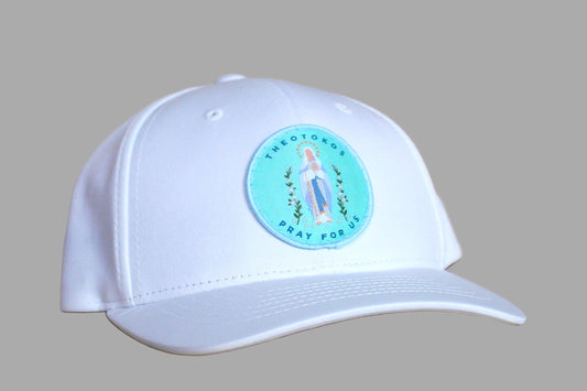 White cap with a circular emblem featuring a religious figure on a wooden surface