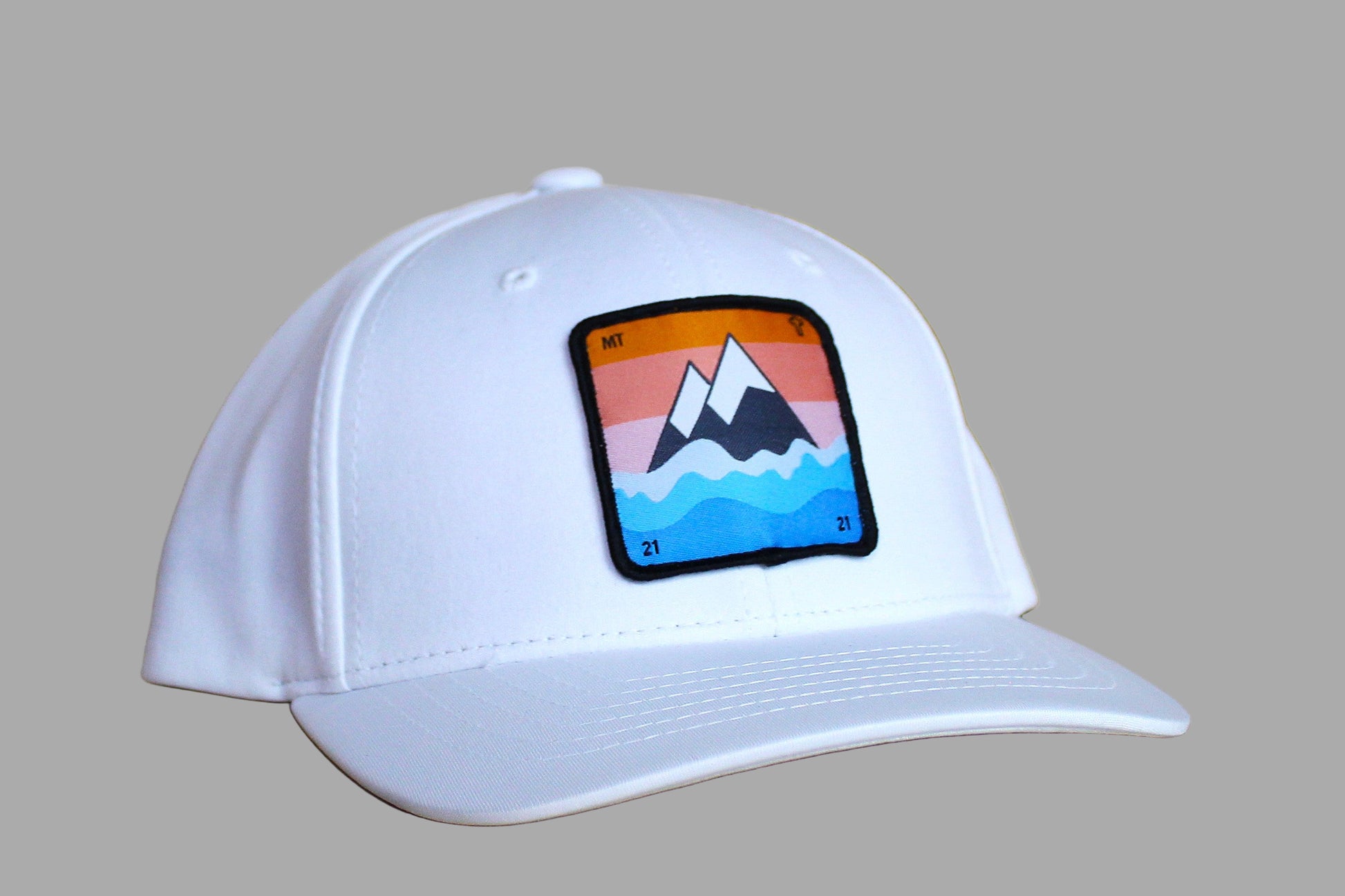 White cap with a colorful mountain patch on a wooden surface
