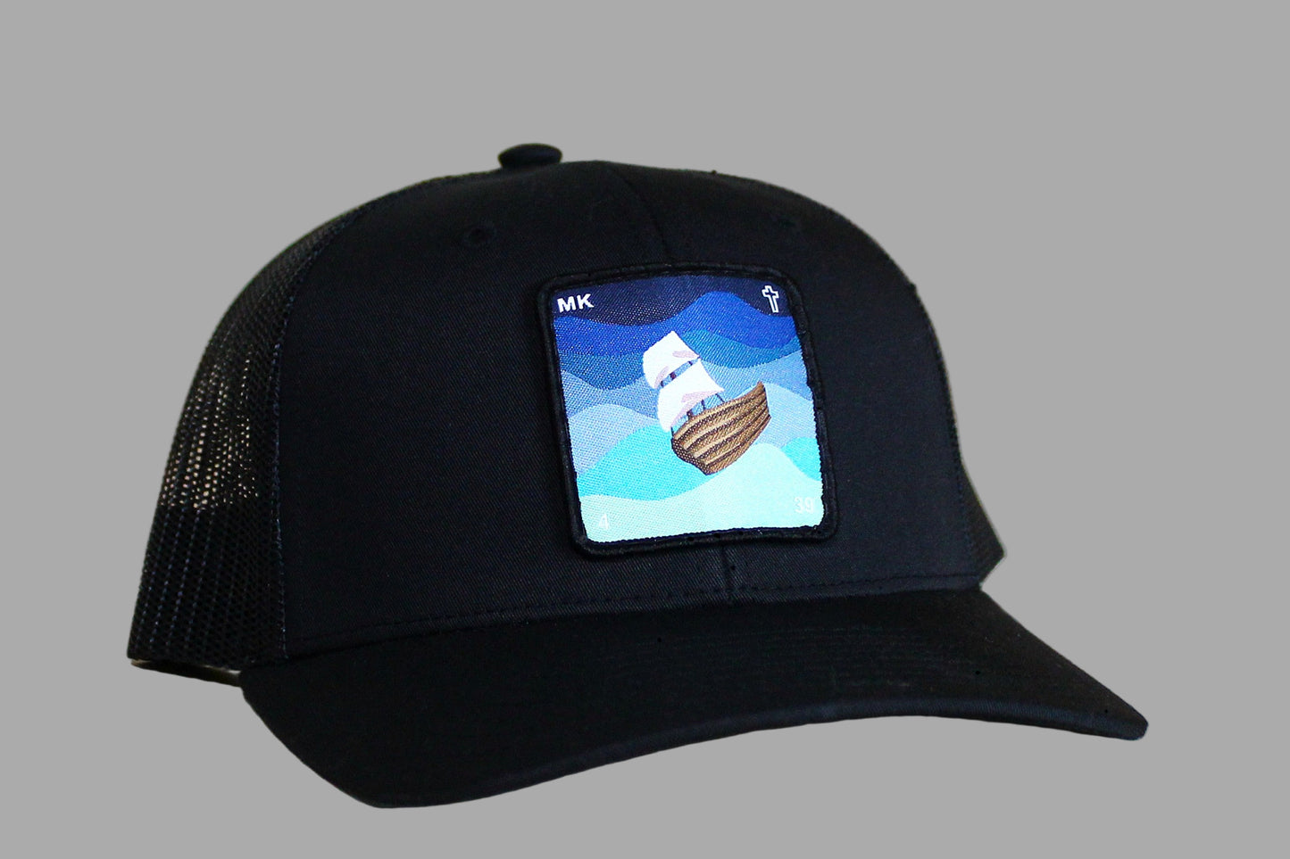 Black cap with a embroidered design of a ship on a wooden surface