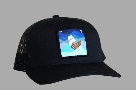 Black cap with a embroidered design of a ship on a wooden surface
