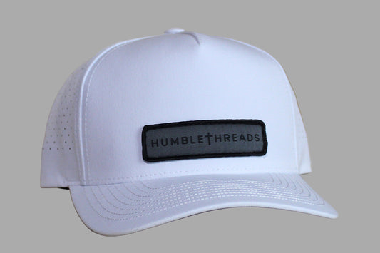 White cap with a black patch labeled 'Humble Threads' on a wooden surface