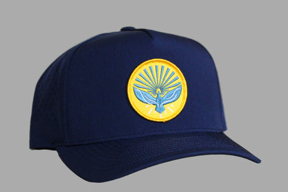 Navy blue cap with a yellow emblem featuring a bird design on a light wooden background