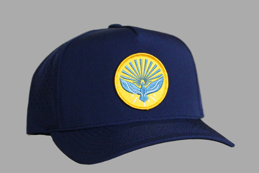 Navy blue cap with a yellow emblem featuring a bird design on a light wooden background