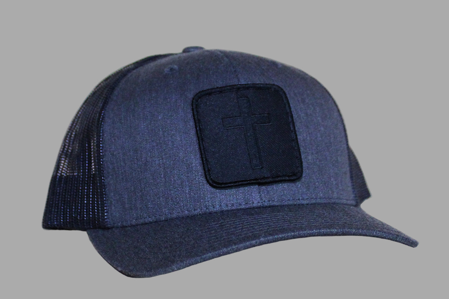 Blue trucker cap with a black patch featuring a cross on a light wooden surface.